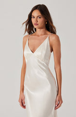 A woman is wearing a sleeveless, satin dress with thin, beaded shoulder straps. The dress is ivory-colored, with a V-neckline and a fitted silhouette.