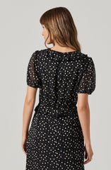 A woman is wearing a black dress with a pattern of small, light-colored polka dots. The dress has short, puffed sleeves and a ruffled collar.