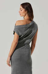 A woman is wearing a fitted, sleeveless, gray knit dress with a unique off-the-shoulder design on one side. The dress has a draped, relaxed fit on the top, and the fabric appears soft and textured. She is accessorized with small hoop earrings and a ring on her left hand, and has shoulder-length brown hair styled in loose waves.