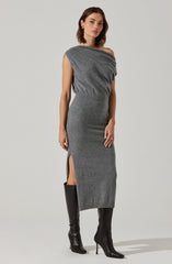 A woman is wearing a gray, one-shoulder, midi-length dress with a side slit. The dress appears to be made of a soft, knit fabric that fits snugly around her body. She pairs the dress with tall black heeled boots.