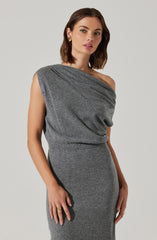 A woman is wearing a sleeveless, one-shoulder gray knit dress with a draped top that has a relaxed fit and a fitted skirt. She accessorizes with gold earrings and rings.
