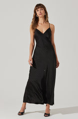 A woman is wearing a black, floor-length dress with thin spaghetti straps. The dress features a subtle pattern of small, evenly spaced, light-colored dots. The fabric appears silky and smooth, giving it an elegant and dressy appearance. She is also wearing black open-toe high heels.