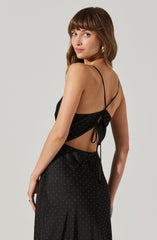 A woman is wearing a black, spaghetti strap dress with small white polka dots. The dress has a cut-out back with a tie detail at the waist.