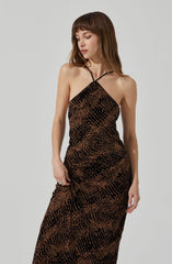 A woman is wearing a sleeveless, full-length dress with a black and brown snakeskin pattern. The dress has a fitted silhouette with a halter neckline and thin black straps crossing at the shoulders.