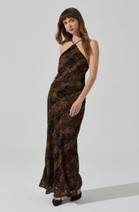 A woman is wearing a long, sleeveless, form-fitting dress with a black and brown animal print pattern. The dress has a halter neckline with a thin strap that goes around her neck, leaving her shoulders and arms bare. She is also wearing black high-heeled shoes.