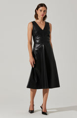 A woman is wearing a sleeveless black dress made of shiny material, featuring a V-neckline, a fitted bodice, and a high-waisted, A-line skirt that falls below the knees. She has on black pointed-toe high heels.