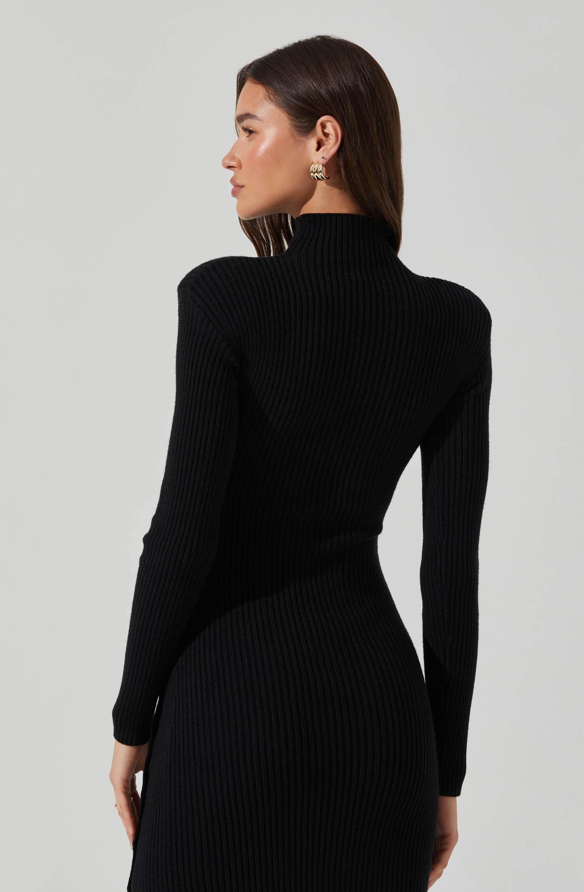 A woman is wearing a fitted, long-sleeve, black ribbed turtleneck dress that extends to her knees.