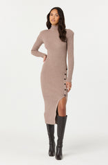 A woman is wearing a long, ribbed knit dress in a light beige color. The dress features a high neckline and long sleeves. It has a side slit that reaches just above the knee, with a row of dark buttons running down one side from the waist to the hem. She is also wearing tall black boots.