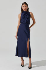 A woman is wearing a sleeveless, high-neck, navy blue satin dress. The dress has a gathered, draped bodice and a fitted waist. The skirt is long and features a side slit that reveals one leg. She is also wearing black high heels with decorative embellishments on the toes.