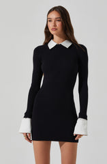 A young woman is wearing a fitted, long-sleeve, ribbed black dress with white collar and cuff accents.