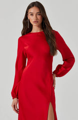 A woman is wearing a long, red satin dress with long sleeves and elasticized cuffs. The dress has a high, rounded neckline and features a high slit on one side. She is accessorized with long, dangling earrings.