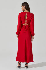 A woman is wearing a long, bright red dress with long sheer sleeves that are gathered at the wrists with elastic. The back of the dress features a keyhole opening at the upper back, and a ruched bodice with a lace-up tie detail at the waist, revealing some skin. The dress has a floor-length, flowing skirt. She is also wearing black high-heeled sandals with ankle straps.