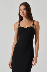 A woman is wearing a fitted black dress with thin, decorative spaghetti straps tied into bows at the shoulders. The dress features a sweetheart neckline with a scalloped edge detail along the bust.