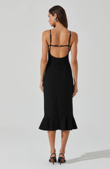 A woman is wearing a black, sleeveless, midi-length dress with thin spaghetti straps. The dress features an open back with multiple black straps across the upper back and shoulders, creating a strappy design. The lower part of the dress has a ruffled hem, adding a flouncy detail to the bottom.