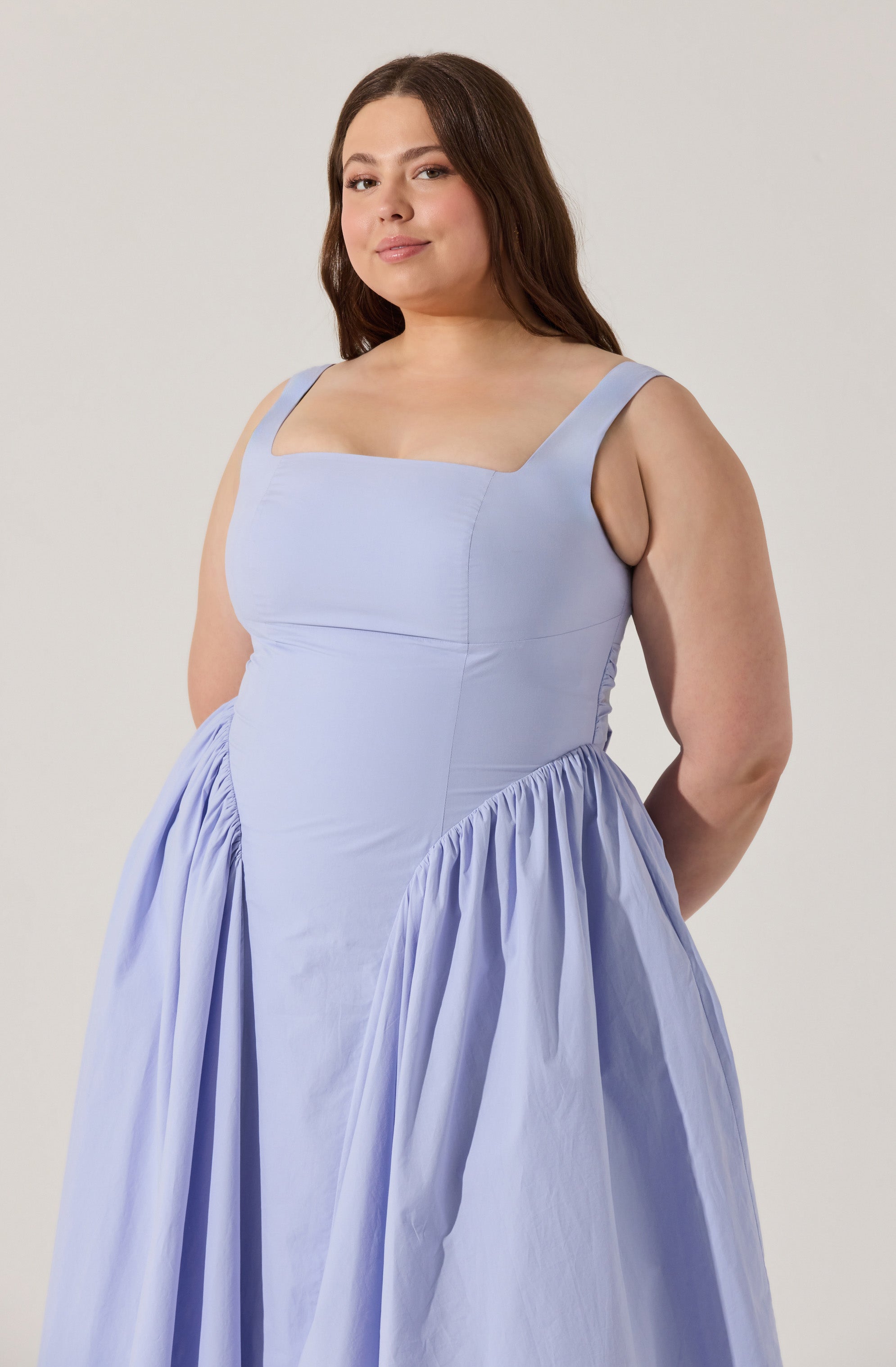 A woman is wearing a sleeveless, light blue dress with wide straps, a fitted bodice, and a full, gathered skirt. The dress appears to be made of a smooth fabric with a slight sheen.