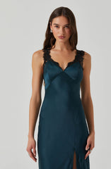 A woman is wearing a teal satin slip dress with black lace straps and trim along the neckline and shoulders. The dress features a fitted bodice with a subtle V-neckline and a thigh-high slit on the side.