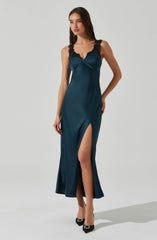 A woman is wearing a long, satin-like teal dress with black lace shoulder straps. The dress features a deep V neckline with a wrap detail at the bust and a high slit on one side, revealing her leg. She is also wearing black high heels with decorative embellishments.