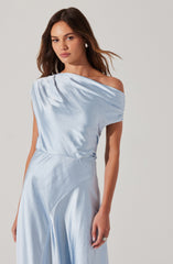 A woman is wearing a light blue satin dress that features an off-the-shoulder design on one side, with the fabric draping elegantly over her shoulder and upper arm. The dress has a smooth, shiny texture with a fitted waist and a flowing, wide-leg skirt.