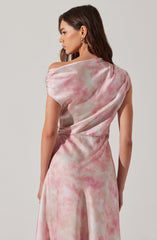 The dress is a sleeveless, flowing gown with a one-shoulder design. It features a soft, watercolor-like pattern in shades of pink, cream, and light gray, creating a delicate and elegant appearance. The fabric appears to be smooth and silky, with gentle draping and subtle gathers.