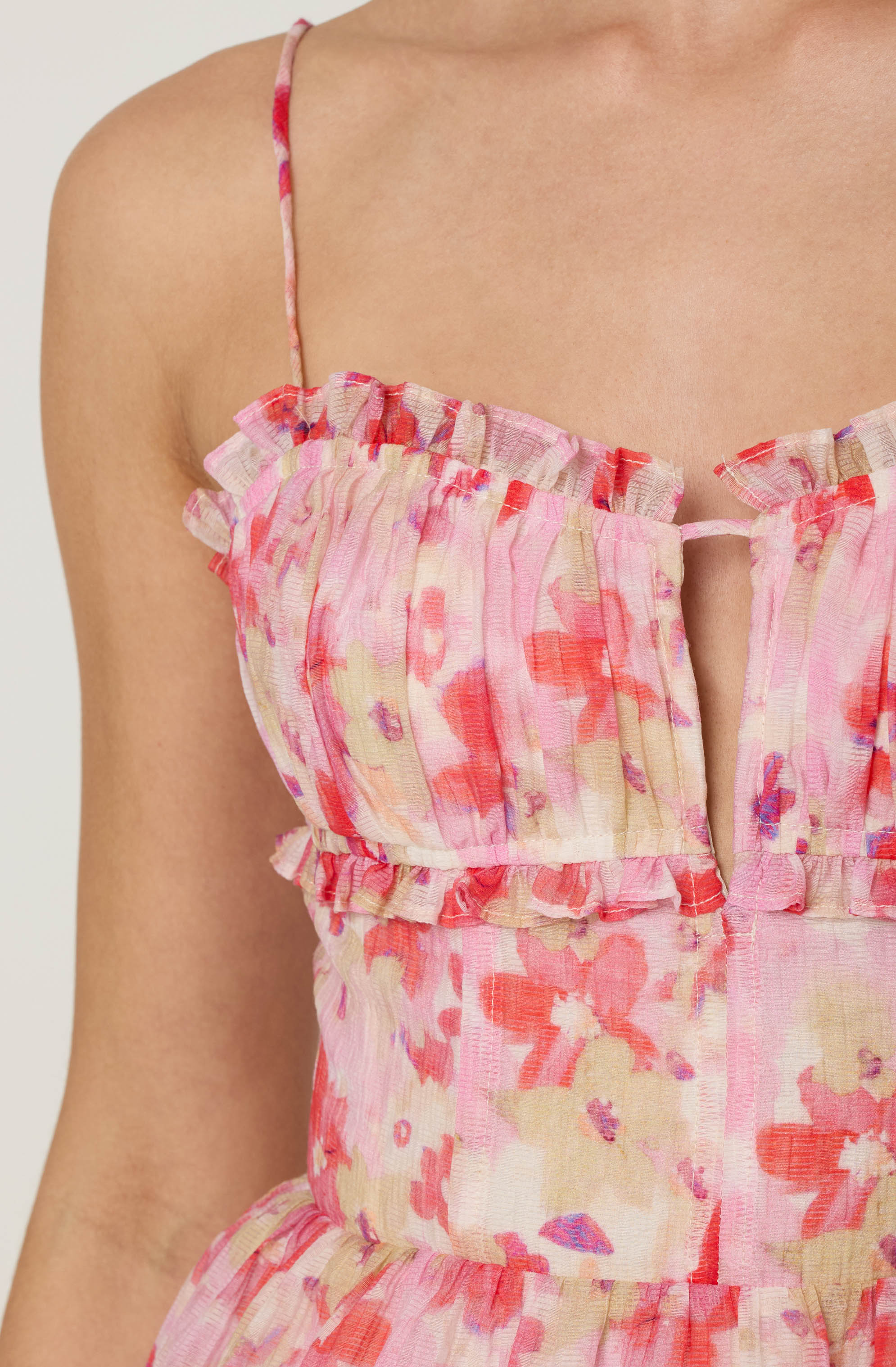 A sleeveless dress with a pink, red, and cream floral pattern. The dress features thin spaghetti straps, ruffle details along the neckline, and a fitted waist. The fabric appears lightweight and slightly textured.