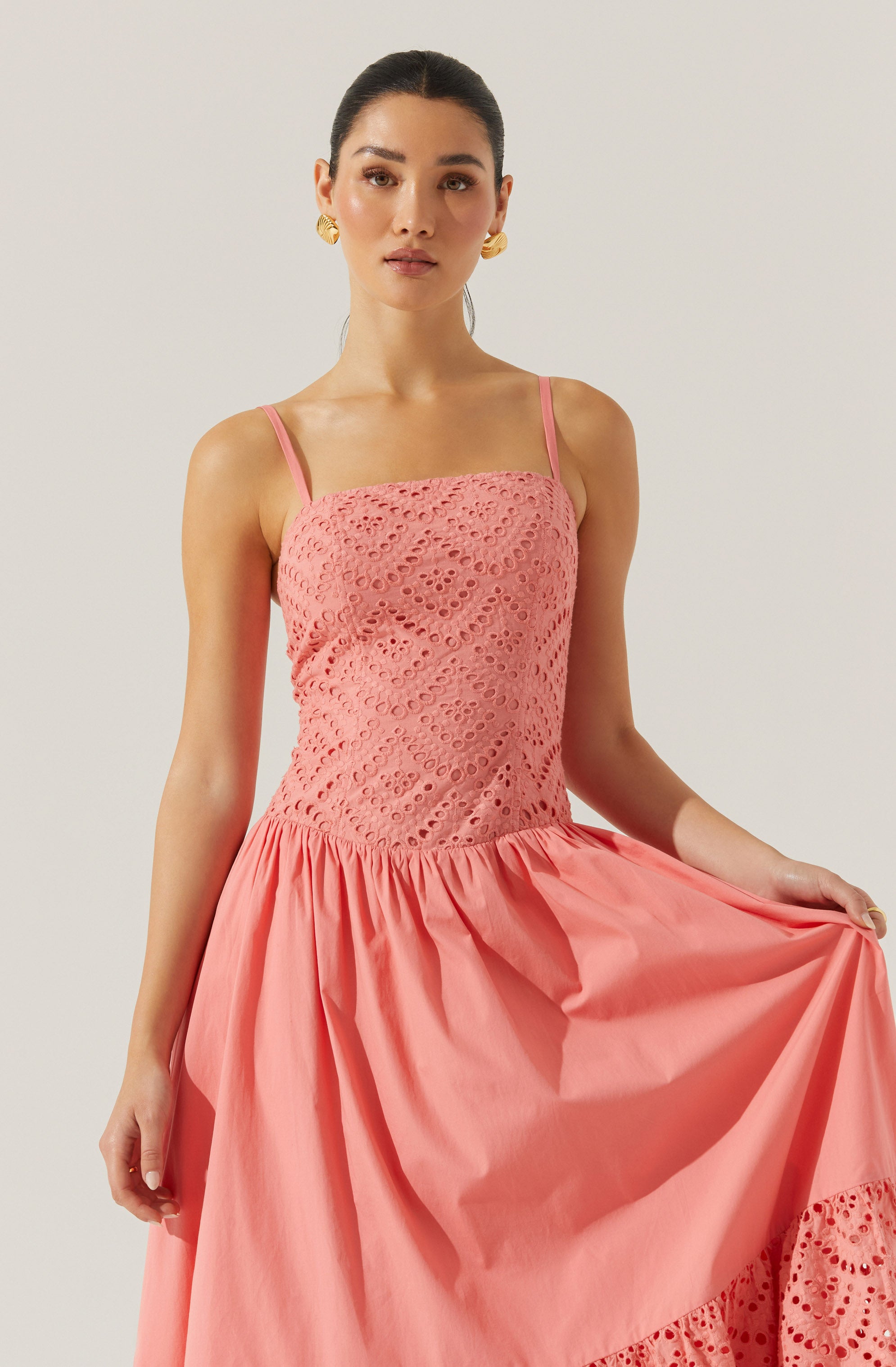 The dress features a sleeveless design with thin shoulder straps. The bodice is made of pink lace fabric with a circular cut-out pattern. The skirt is made of solid pink fabric, gathered at the waist, and has decorative lace detailing near the hem.