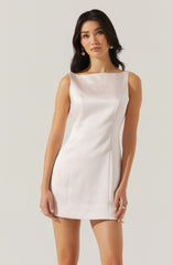 A woman is wearing a sleeveless, knee-length, ivory-colored dress with a boat neckline and a tailored fit. The fabric appears smooth and slightly shiny, giving it an elegant look.