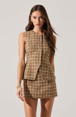 A woman is wearing a sleeveless, fitted top and skirt set made of a textured, plaid fabric in shades of brown, beige, and green. The top has a structured, tailored fit with a round neckline and a front opening that appears to be fastened with buttons. The skirt is short and fitted, matching the fabric of the top. The overall outfit has a classic, sophisticated look with a checkered pattern.
