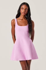 A woman is wearing a sleeveless, pastel pink dress with thick straps, a fitted bodice, and a flared skirt that falls above the knees.