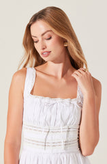 A sleeveless white dress with lace trim on the straps and neckline, featuring gathered fabric and subtle embroidery details around the waist.