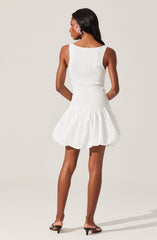 A woman is wearing a sleeveless, fitted white top with a round neckline and a voluminous, bubble-style white skirt that has a gathered, puffy appearance.