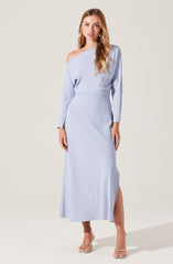 A woman is wearing a long, light blue dress with an asymmetrical neckline that drapes over one shoulder. The dress has long sleeves and a slit up one side, revealing her leg. She is also wearing high-heeled sandals with thin straps.