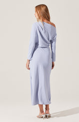 A woman is wearing a light blue, long-sleeved, off-the-shoulder dress with a loose, draped top and a fitted waist. The dress has a silky, flowing fabric and reaches down to her ankles. She is wearing beige high-heeled sandals.