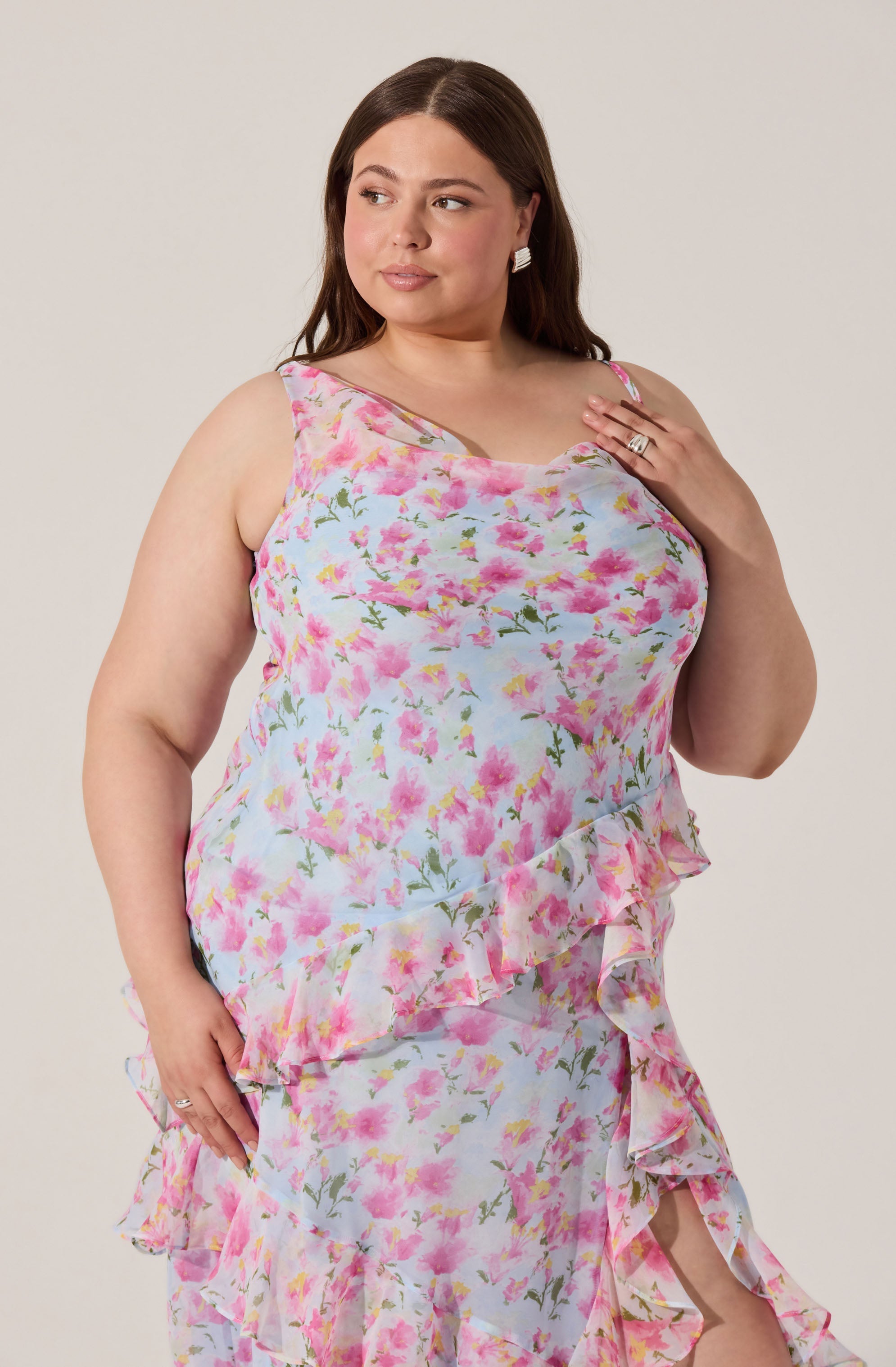 A woman is wearing a sleeveless, floral dress with pink and green flowers on a light pastel background. The dress features ruffled tiers along the sides and bottom.
