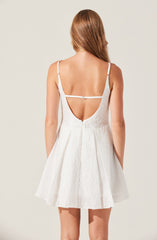 A woman is wearing a sleeveless white dress with adjustable spaghetti straps. The dress features a deep V-back with a horizontal strap across the upper back, and it has a textured fabric with a slight sheen. The skirt is flared, creating an A-line silhouette.
