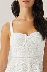 A woman is wearing a white dress with intricate lace patterns. The dress has a fitted bodice with a straight neckline and features lace detailing throughout. It has thin spaghetti straps over her shoulders.