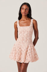 A woman is wearing a sleeveless, peach-colored dress with a floral lace overlay. The dress has a square neckline and features intricate flower patterns throughout. The skirt is slightly flared, creating a A-line silhouette.