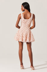 A woman is wearing a sleeveless, pale pink dress with a textured floral pattern. The dress features a fitted bodice and a flared, knee-length skirt. She is also wearing light pink high-heeled shoes.