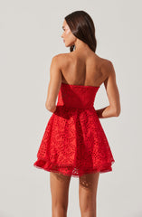 A woman is wearing a strapless, red dress with a fitted bodice and a flared skirt. The fabric features a pattern of small, circular cutouts, creating a semi-transparent look. The hemline is decorated with a scalloped lace trim.
