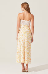 A woman is wearing a sleeveless, fitted top made of white lace fabric with delicate spaghetti straps. She is also wearing high-waisted, wide-leg pants with a light yellow base color and a floral pattern featuring orange and yellow flowers.
