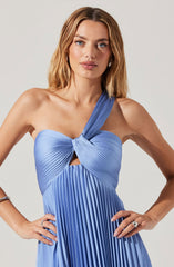 A woman is wearing a stylish, pleated, light blue dress with an asymmetrical design. The dress features a single shoulder strap on her right side that is twisted into a knot at the top, creating a draped effect, while her left shoulder is left bare. The pleats run vertically down the length of the dress, giving it a textured and elegant appearance.