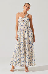 A woman is wearing a sleeveless, long maxi dress with a light beige background and a blue floral print. The dress has a distinctive twisted knot detail at the bust with a small keyhole opening just below it. The skirt is flowing and pleated, creating a soft, airy silhouette.