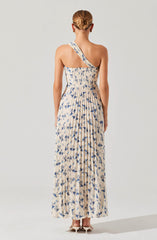 A woman is wearing a long, flowing dress with a beige base color and a blue floral print. The dress features a one-shoulder strap design. The fabric appears lightweight and comfortable, suitable for warm weather. She is also wearing neutral-colored high heels.