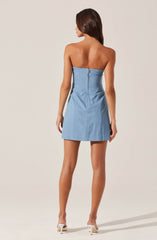 A woman is wearing a strapless, light blue denim mini dress with a visible back zipper closure. She has nude high heels and long, dark brown hair.