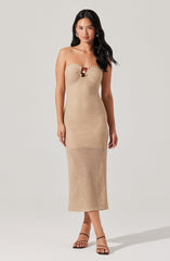 A woman is wearing a strapless, beige, textured knit dress that reaches mid-calf. The dress features a gathered detail at the bust with a small decorative element in the center. She is also wearing black, strappy high-heeled sandals.