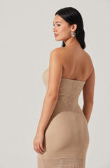 A woman is wearing a strapless, beige, textured, form-fitting dress. She has long, dark hair and is accessorized with large, silver hoop earrings.