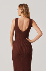 A woman is wearing a sleeveless, knitted dress in a reddish-brown color. The dress features a deep scoop neckline in the back, fitted at the waist and hips, with a textured, open-knit pattern throughout. She has her left arm bent with her hand resting on her hip.