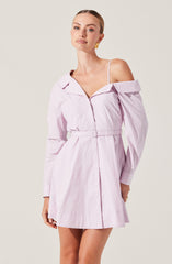 A woman is wearing a light purple, off-the-shoulder dress with a collar and long sleeves. The dress features a matching belt at the waist, and the bodice has a zipper detail in the front. The dress length is above the knees. She is also wearing a white spaghetti strap top underneath.