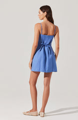 A woman is wearing a blue sleeveless dress with thin spaghetti straps and a waist tie bow. She has on white woven shoes.