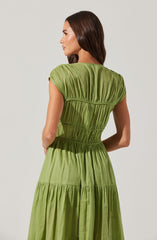 A woman is wearing a light green, tiered dress made of a soft, flowing fabric. The dress features short, gathered sleeves and multiple horizontal seams that create a gathered, textured effect throughout the garment. The waistline is slightly cinched, and the skirt section is gathered with a tiered design.