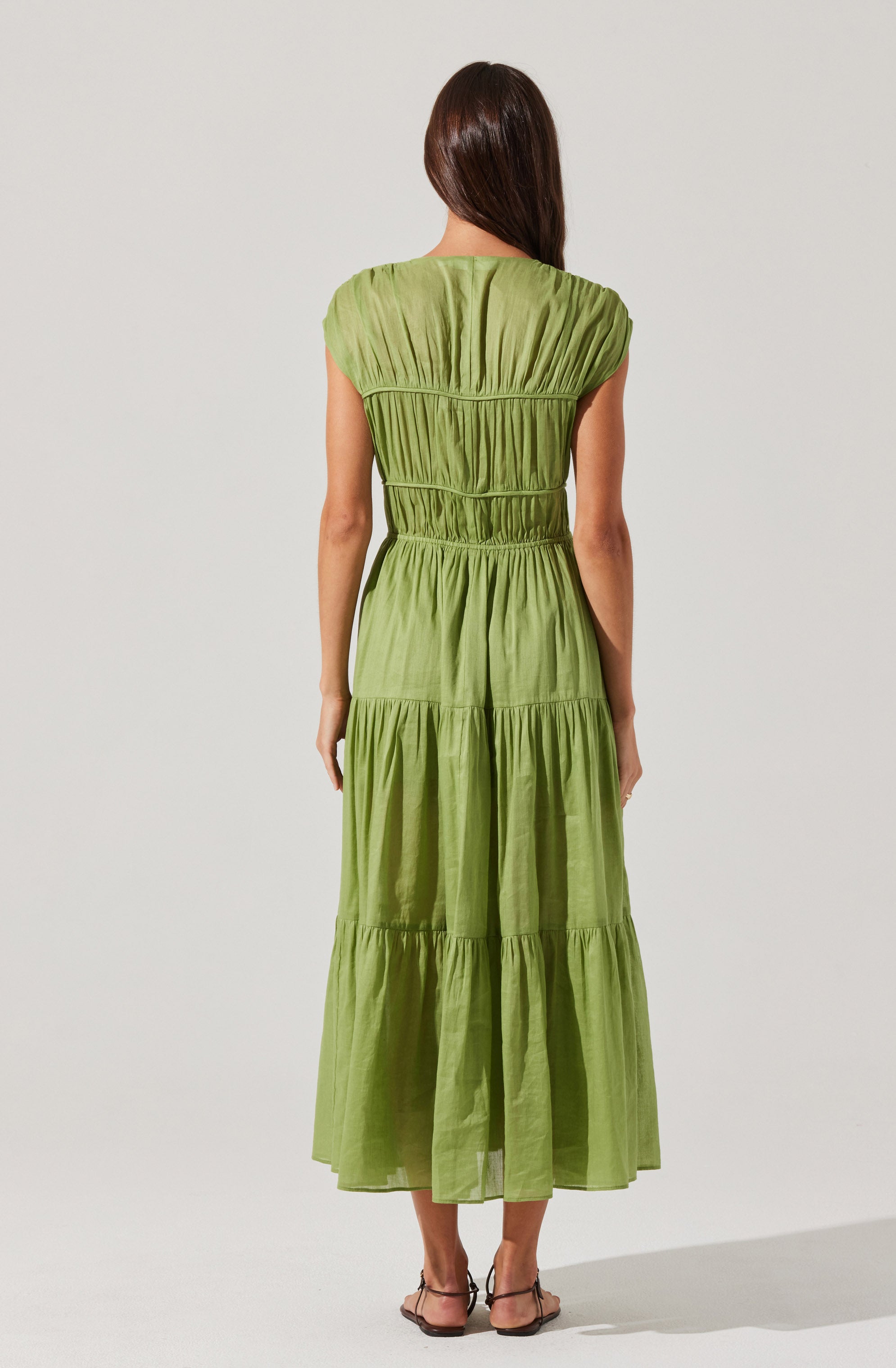The dress is a long, tiered maxi dress in a vibrant lime green color. It features a gathered, ruched bodice with an empire waist and cap sleeves. The fabric has a slight sheen and a lightweight, flowing appearance.